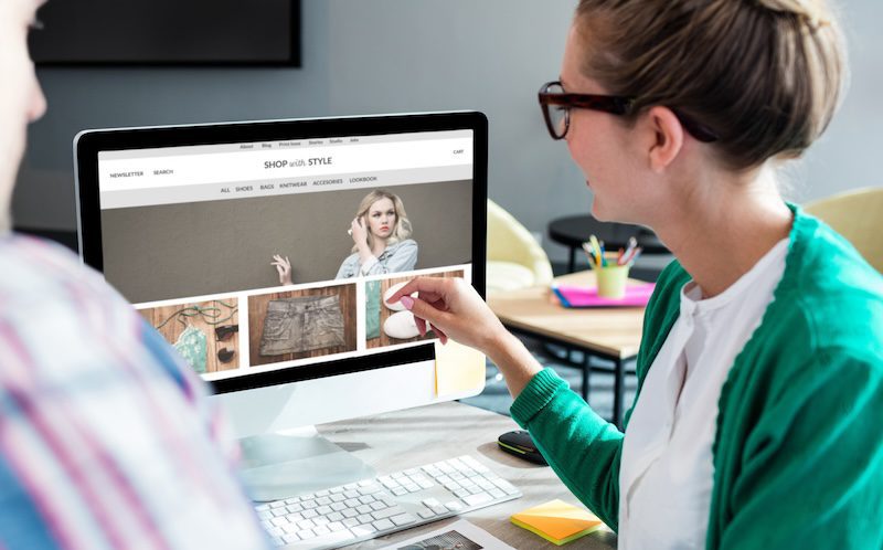 Two people are looking at a fashion website on a desktop computer.