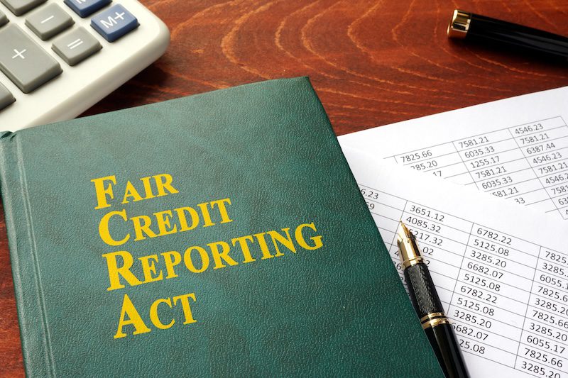 A green book titled "Fair Credit Reporting Act" rests on a wooden table next to a spreadsheet with numbers, a pen, part of a calculator, and documents about the LexisNexis freeze.