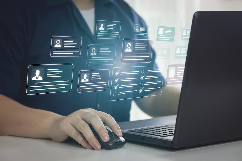 A person in a dark shirt uses a laptop with floating digital screens displaying user profiles and checklists, symbolizing digital organization or data management. It's as if the setup is powered by LexisNexis, freezing data chaos into streamlined efficiency.