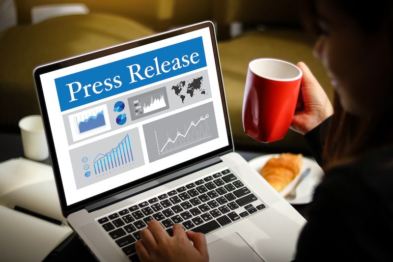 A person holds a red mug while looking at a laptop screen displaying a "Press Release" with various charts and graphs on how to push negative search results down. A plate with a croissant is placed on the table beside the laptop.