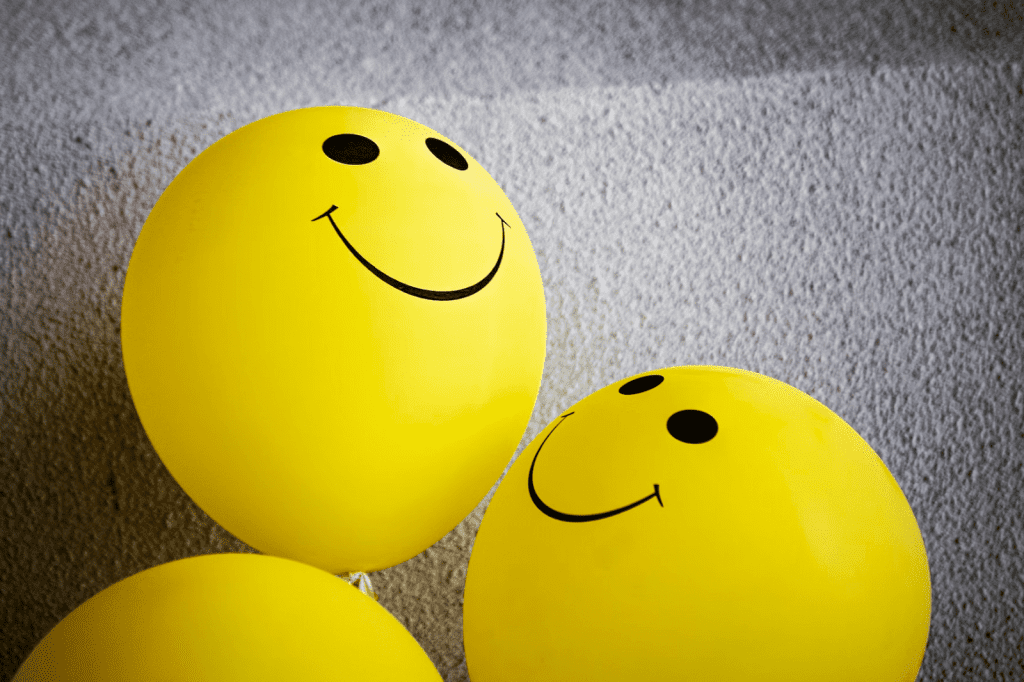 three yellow balloons with a smiley face drawn on them.