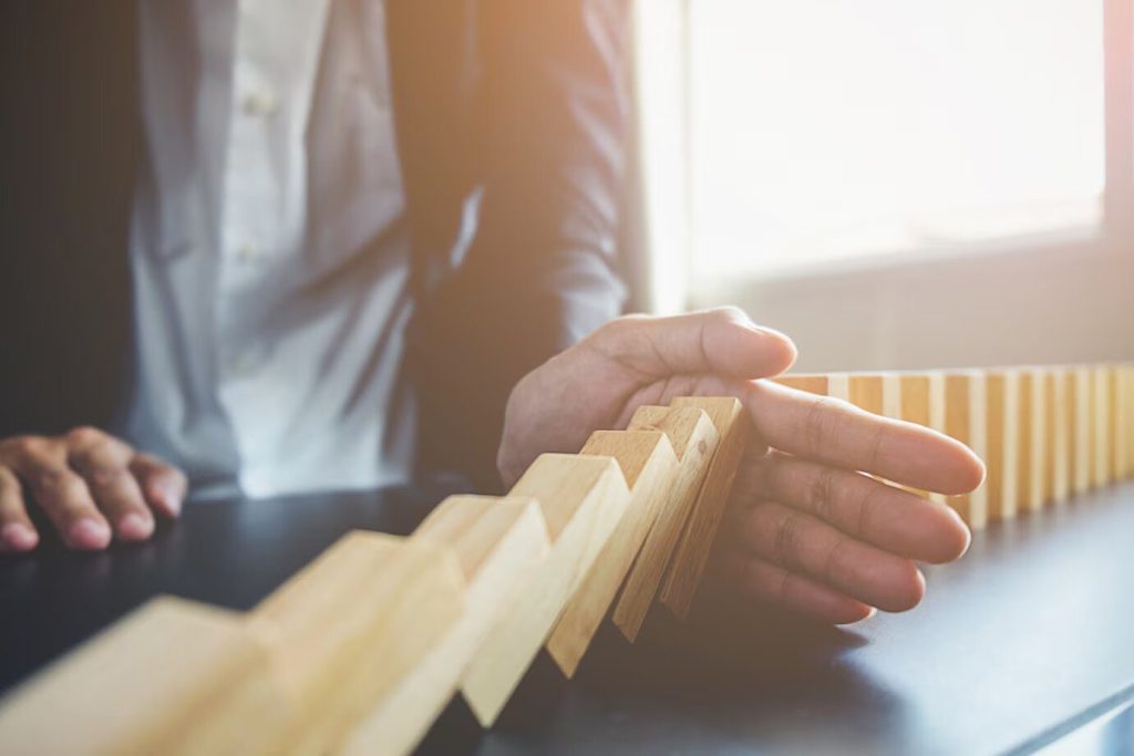 a businessman pushing wooden dominoes in front of a desk.