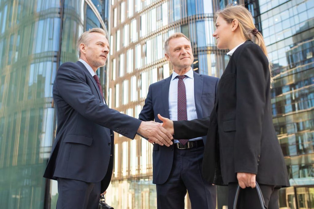 three business people shaking hands in front of an office building.