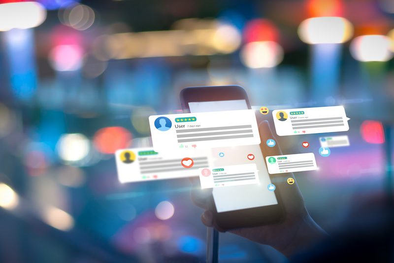 A hand holds a smartphone, displaying multiple floating chat bubbles, reviews, and social media notifications. Among them, a prominent reputation score stands out. The background is blurred with multi-colored bokeh lights, giving a sense of a busy and vibrant digital environment.