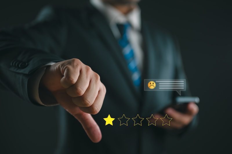 A person in a suit gives a thumbs-down gesture. A one-star rating symbol is shown, with one gold star and four empty stars. A digital icon of a sad face in a speech bubble is displayed near the hand, suggesting dissatisfaction with the reputation score or reflecting a negative review.