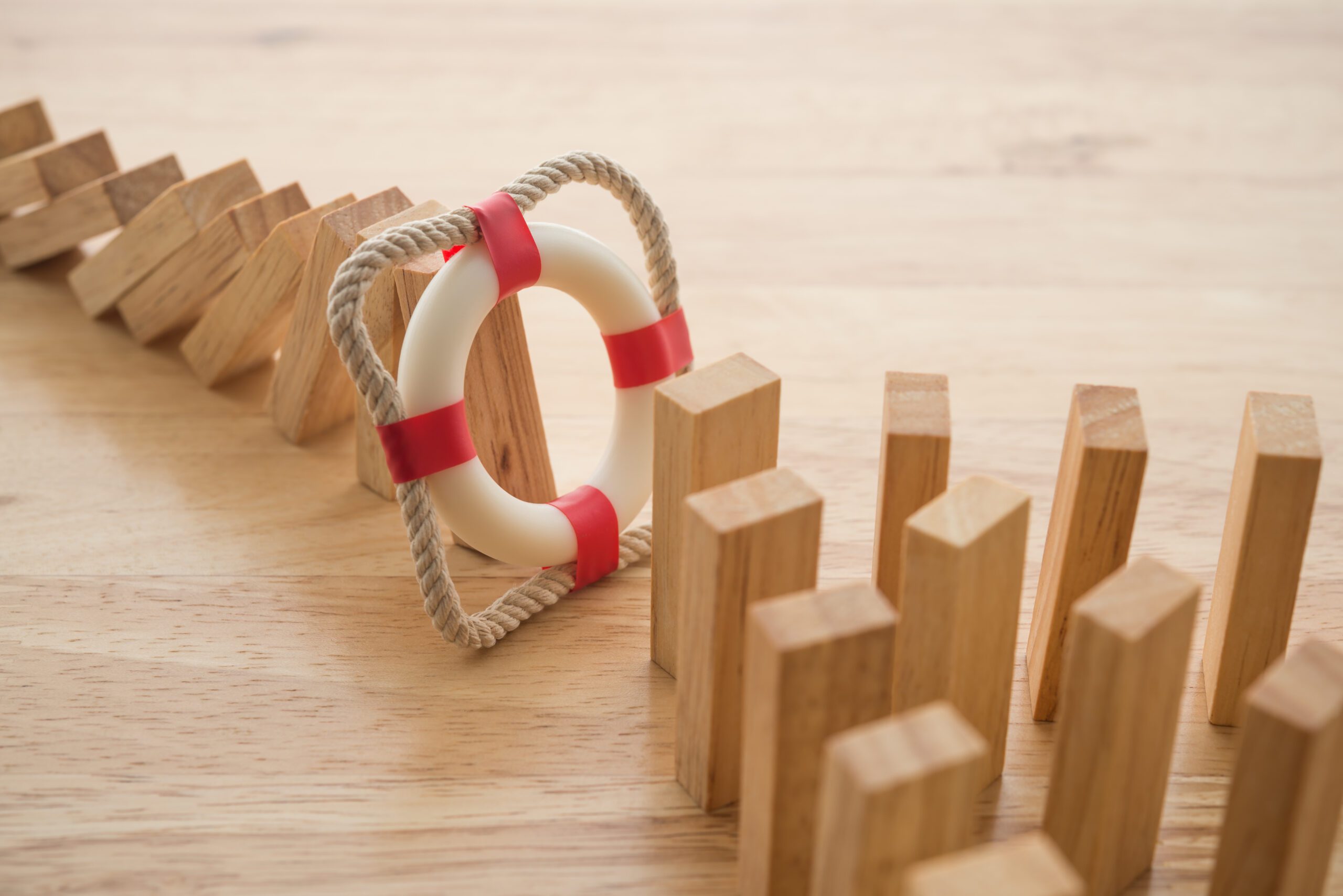 An image showing a toppled sequence of wooden blocks, with a life ring stopping the last block from falling. The life ring, featuring red and white sections with rope around it, symbolizes intervention in crisis and reputation management, preventing the remaining upright blocks from toppling.