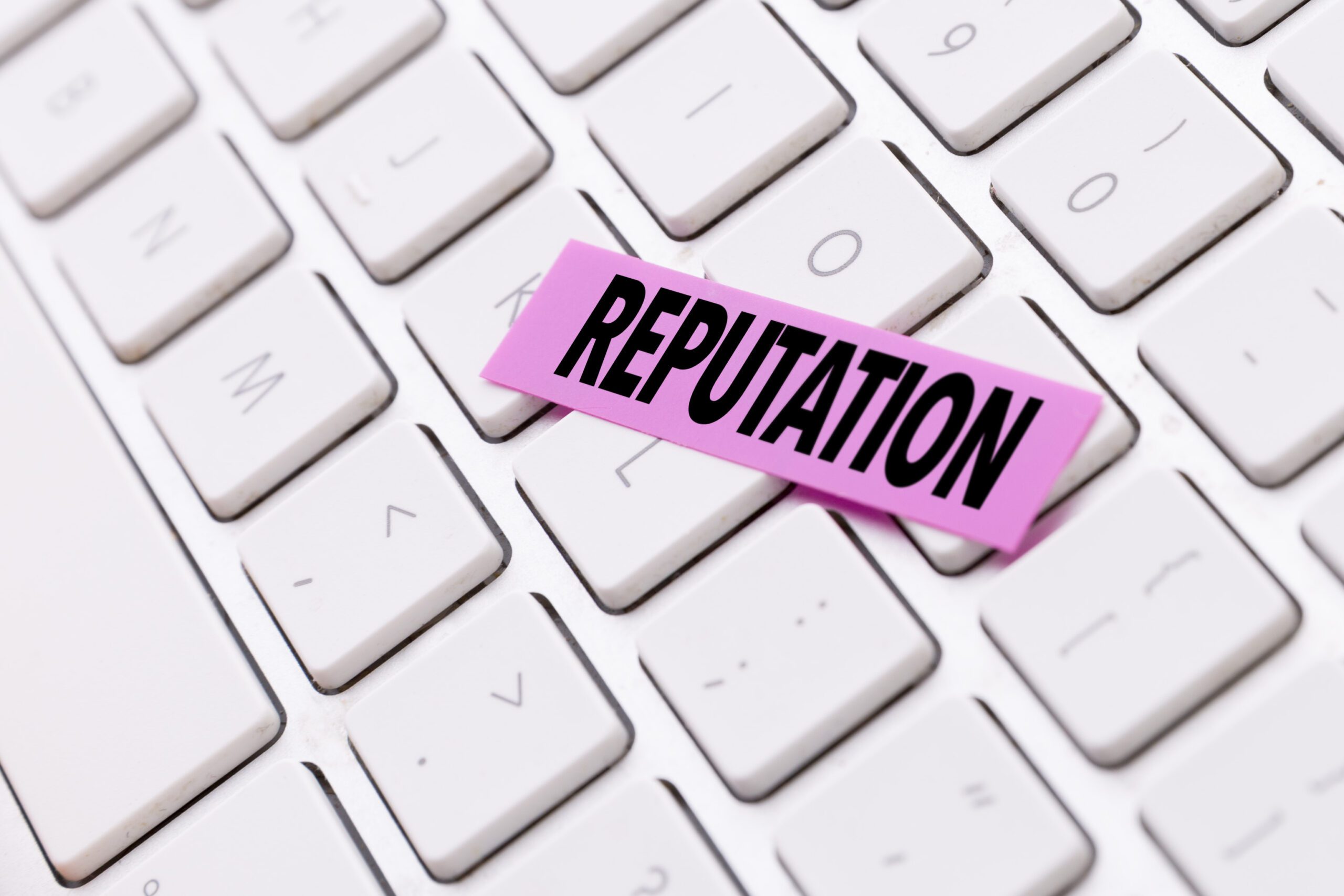 A close-up of a white keyboard with a pink sticky note on top, displaying the word "REPUTATION" in bold, black letters.