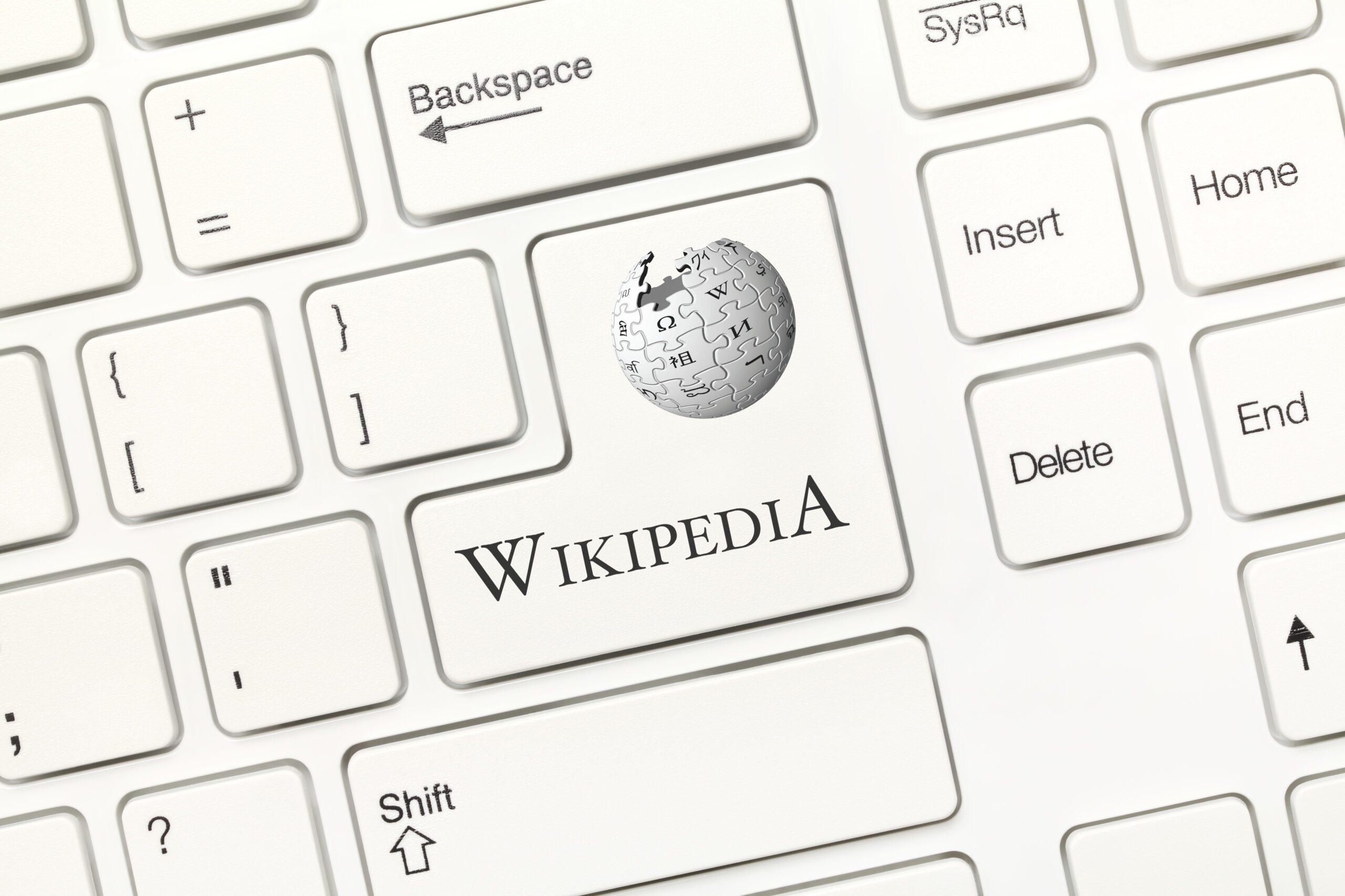 A keyboard with white keys features a unique key where the "Enter" key usually is. This key displays the Wikipedia logo, a puzzle globe, and the word "WIKIPEDIA" instead of the usual key label.