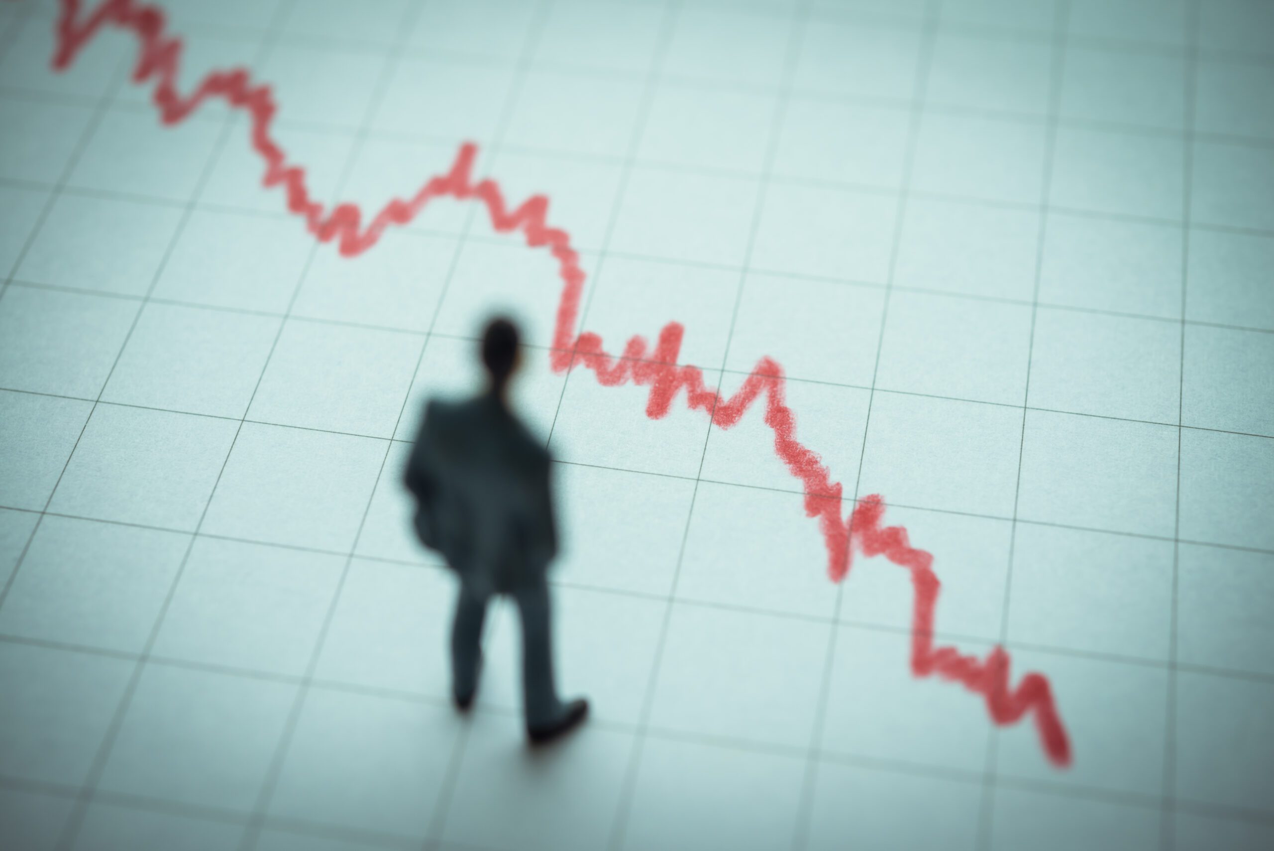 A blurred silhouette of a person in a suit stands in front of a line graph with a red, downward trend, suggesting a decline or loss. The grid background emphasizes the financial theme.